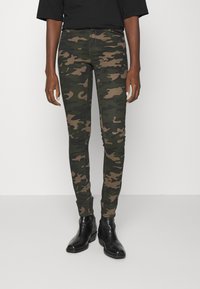 Kameraskjortade skinny jeans i nyanser av grönt och brunt, med en tajt passform, elastiskt material och en klassisk femfickorsdesign. Svarta ankelstövlar.