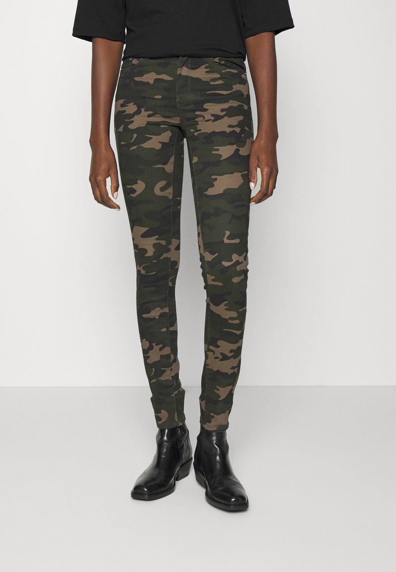 Kameraskjortade skinny jeans i nyanser av grönt och brunt, med en tajt passform, elastiskt material och en klassisk femfickorsdesign. Svarta ankelstövlar.