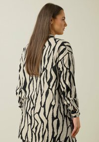 Camisa de manga larga con tejido beige y un patrón de rayas abstractas de cebra en negro, textura suave y puños abotonados.