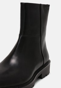 Černá kotníková bota z hladké kůže, s propracovaným designem a robustní podrážkou. Má minimální švy a texturovaný podpatek.