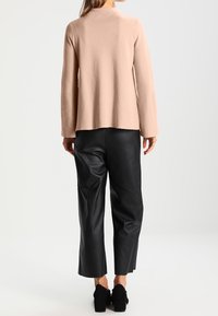 Ljusrosa tröja med långa ärmar och rundad halsringning, kombinerad med svarta läderbyxor med vida ben och svarta klackskor med blockklack.