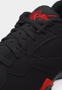 Κοντινό πλάνο μαύρου αθλητικού παπουτσιού με πλευρική επιφάνεια από δίχτυ, μαύρα κορδόνια και κόκκινο χαρακτηριστικό λεπτομέρειας στη γλώσσα και στην έμφαση της σόλας.