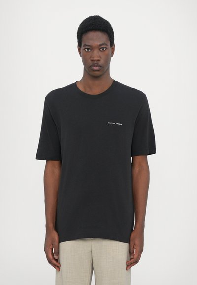 T-shirt en coton noir à manches courtes et col rond, avec un petit logo blanc sur la partie gauche de la poitrine. Ourlet inférieur droit.