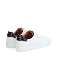 Baskets en cuir blanc avec des accents texturés noirs au niveau du talon, bout rond, à lacets à l'avant, et semelles en caoutchouc. L'intérieur est doublé de tan.