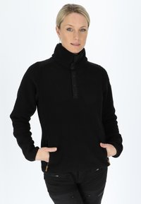 Pullover in pile nero con colletto alto, chiusura frontale a bottoni e tasche laterali. Presenta un tessuto testurizzato e dettagli a contrasto.