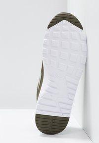 Semelle d'une chaussure Nike avec bande de roulement blanche et vert olive montrant un motif texturé pour une meilleure adhérence et un logo en relief.
