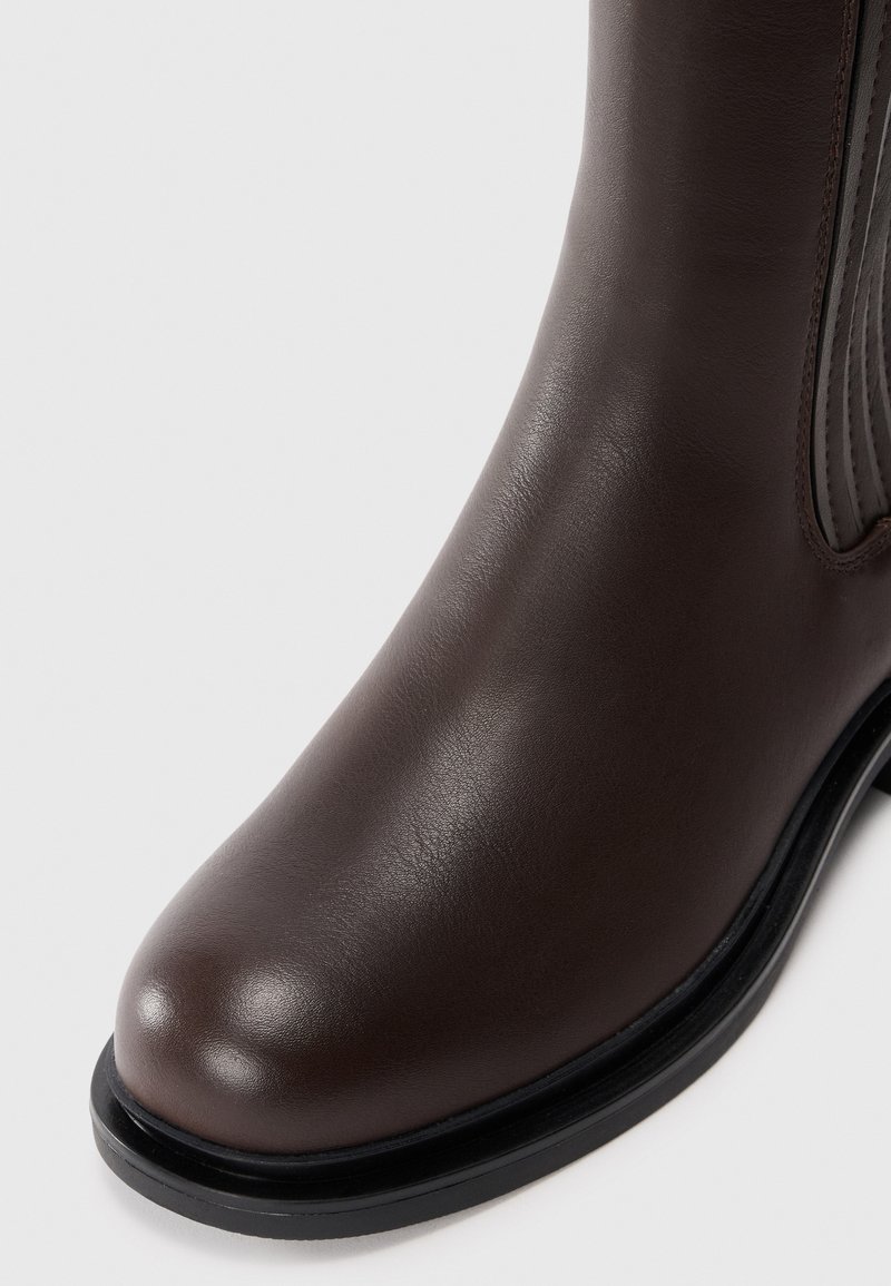 Stivale alla caviglia in pelle marrone con superficie liscia, punta arrotondata e suola in gomma nera. Presenta pannelli laterali elasticizzati per facilitarne l'indossamento.