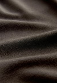 Lähivaade pehmest, tumepruunist kangast, mille peen kudumistruktuur ja õrnad voldid loovad pehmeid varje.