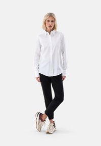 Weißes Hemd mit Knöpfen, schwarze Hose und mehrfarbige Sneakers. Glatter Stoff, lange Ärmel und taillierte Passform. Lässiger, aber professioneller Look.