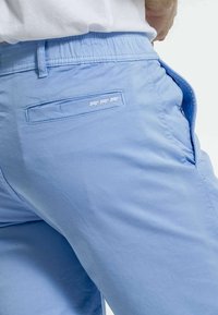 Shorts bleu clair en tissu lisse, dotés d'une taille élastique, de poches latérales et d'une poche arrière avec un détail de logo.