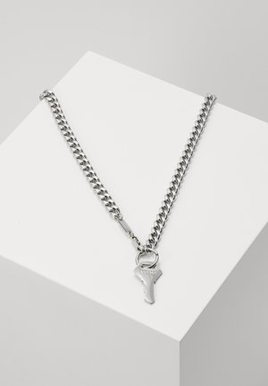 Collier chaîne en argent avec des maillons épais et un pendentif en forme de clé gravé de "VITALY" présenté sur une surface blanche en angle.