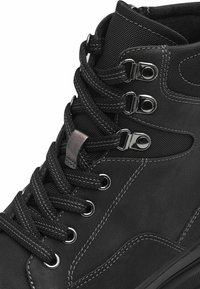 Basket noire montante en cuir et maille, avec des œillets métalliques, des lacets épais et des coutures contrastées.