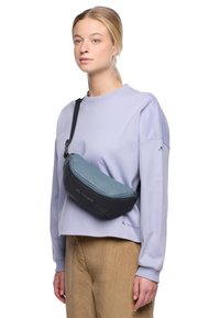 Sac bandoulière noir et bleu canard avec une forme incurvée, fabriqué en tissu texturé. Il présente une bandoulière adjustable et un détail de logo sur le côté.