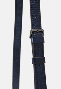 Ceinture en cuir bleu marine avec une finition texturée, dotée d'une boucle en métal argenté et de plusieurs trous d'ajustement le long de la sangle.