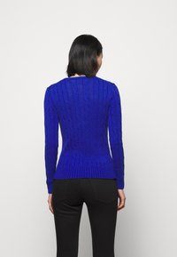 Blå kabelstickad tröja med långa ärmar, ribbad nederkant och strukturerad design; kombinerad med svarta tajta byxor.