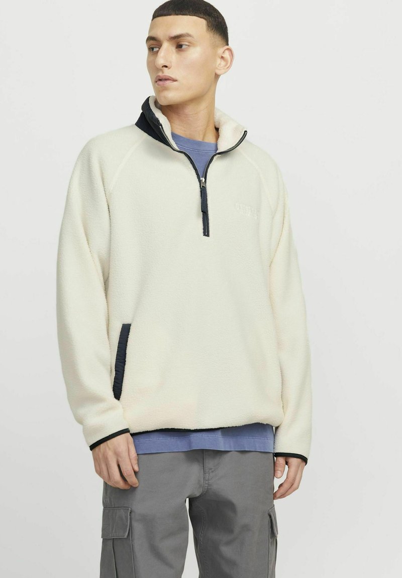 Fleece-Pullover in Off-White mit hohem Kragen und schwarzen Akzenten. Verfügt über einen Viertelreißverschluss und seitliche Taschen. Sanfte Textur.