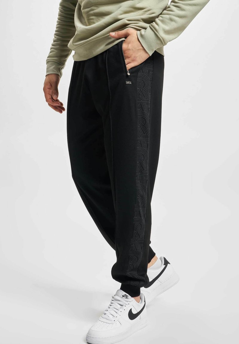 Sorte joggebukser med en tapered fit, med et teksturert logo-print langs siden. Kombinert med hvite sneakers for kontrast.