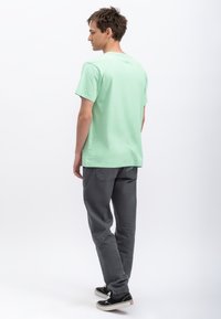 T-shirt vert menthe à manches courtes en coton, associé à un pantalon gris foncé. Le t-shirt présente un design simple et une coupe décontractée.