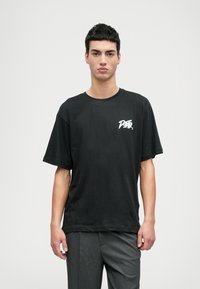 Schwarzes, kurzärmliges Baumwoll-T-Shirt mit lockerer Passform und einem weißen Grafiklogo auf der linken Brust. Einfaches Design, minimale Details.