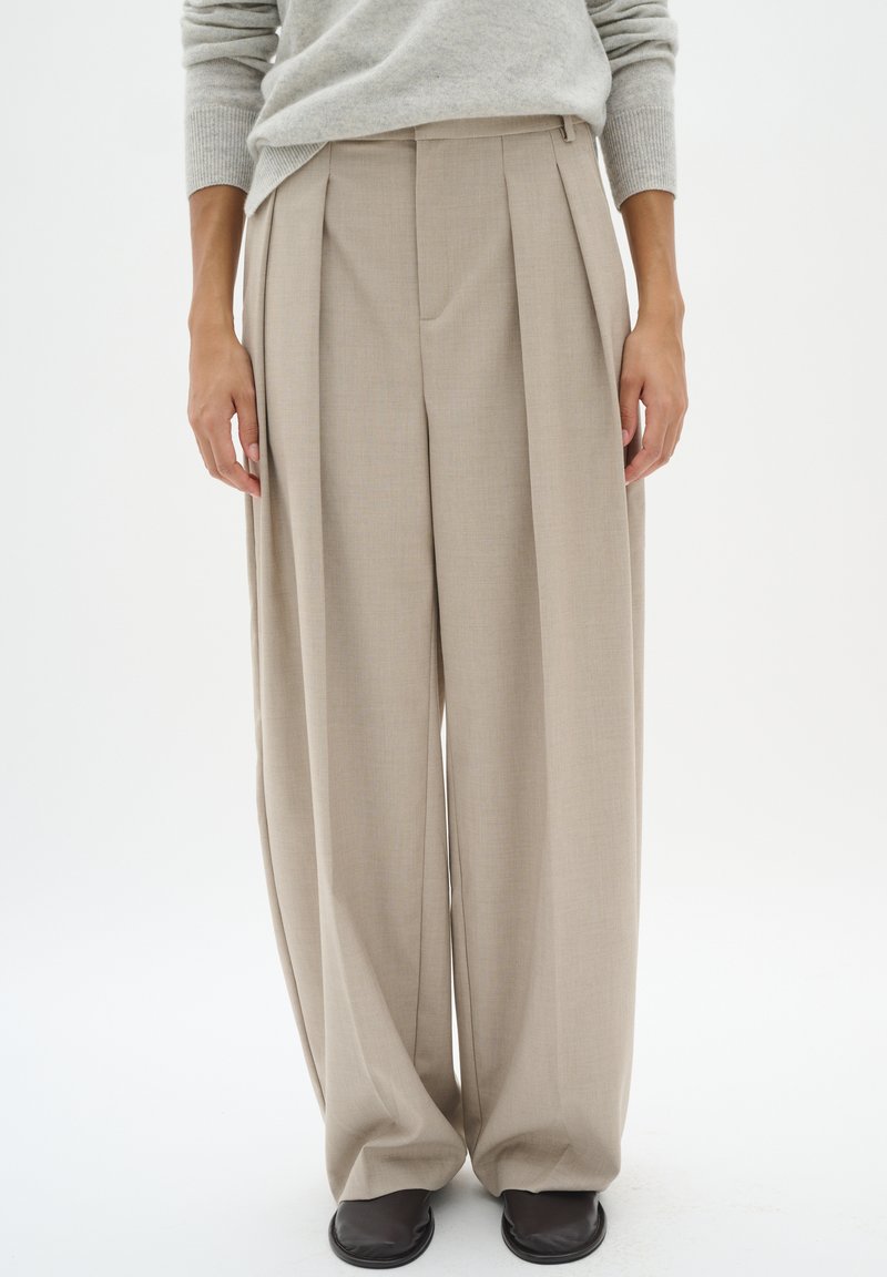 Pantaloni beige plissettati con una vestibilità ampia, realizzati in tessuto texture. Vita su misura e dettagli di pieghe sottili migliorano il design.