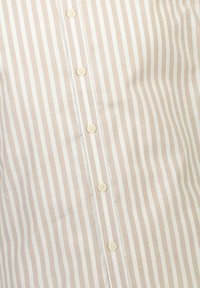 Raidallinen paita vaaleanbeigellä ja valkoisella, jossa on nappuluukku kerma-napeilla, sileä kangas ja hienostunut kiilto. Häivytysviivat ovat voimakkaat.