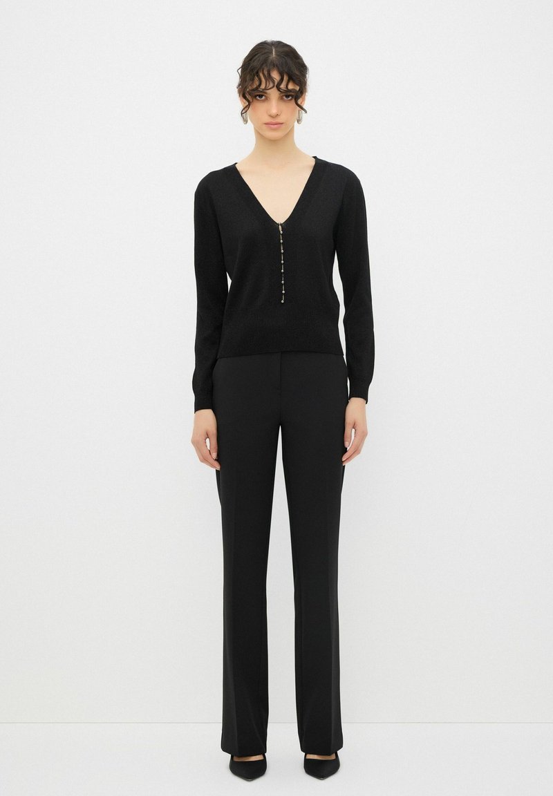 Maglione nero a maglia con scollo a V e maniche lunghe, caratterizzato da una fila di bottoni decorativi lungo la parte anteriore. Abbinato a pantaloni neri su misura.