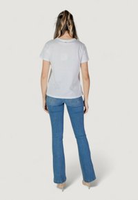 Camiseta de algodón blanca de manga corta y escote redondo, combinada con jeans acampanados de un azul claro. Ajuste casual con una textura suave.
