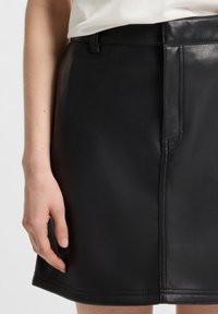 Black leather mini skirt with a smooth texture, featuring a straight cut, belt loops, and visible stitching details.