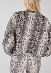 Krótkie, czarno-białe sweter w wzór węża, charakteryzujący się luźnym fasonem, miękką fakturą oraz wysokim kołnierzem, w połączeniu z pasującymi legginsami.