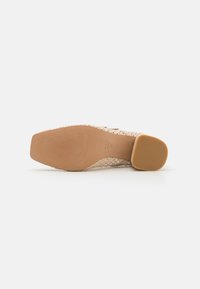 Chaussure tissée beige avec un dessus texturé, un bout carré et un talon carré marron clair. La semelle présente des motifs nervurés pour une meilleure adhérence.
