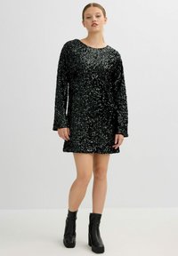 Vestido negro de lentejuelas con mangas largas, escote redondeado y un corte holgado, combinado con botas negras de tacón hasta la rodilla. Textura suave.