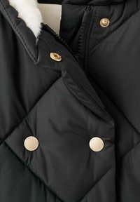 Schwarze gesteppte Jacke mit einem Kunstfellfutter, Reißverschluss und goldenen Hardware-Akzenten an den Knöpfen. Glatte Textur mit Rautenmuster.