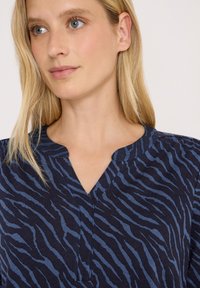 Haut à motif marin avec un décolleté en V, présentant des rayures de zèbre bleues. Fabriqué en matière douce avec une coupe décontractée et des manches courtes.