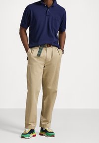 Námořnická polo košile s krátkým rukávem a kapsou, doplněná béžovými kalhotami a vícerozměrnými teniskami se námořnickými, zelenými a červenými akcenty.