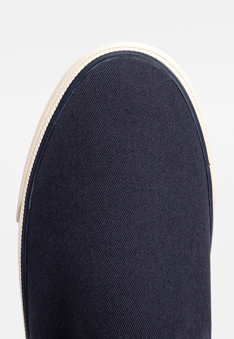 Bottines en toile marine à enfiler avec une surface texturée, semelle en caoutchouc crème contrastante et bout arrondi. Présente des coutures le long du bord.