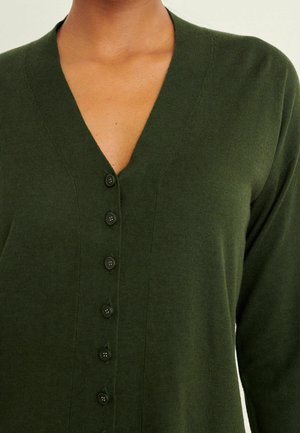Tmavě zelený kardigan s véčkovým výstřihem, s šesti černými knoflíky na přední straně. Tkanina vypadá texturovaně a je přiléhavá.
