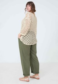 Pull en tricot beige à mailles ouvertes avec des manches trois-quarts, associé à un pantalon ample vert olive et des sandales plates, affichant un design et une texture décontractés.