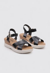 Sandalias de cuña de cuero negro con correas cruzadas y una suela de goma ligera. Cuentan con una correa ajustable en el tobillo y plantilla acolchada.