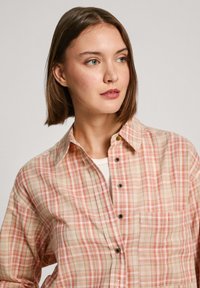 Licht geblokt overhemd in beige, rood en oranje tinten. Katoenen stof, met knopen, voorzien van een borstzak en een relaxte kraag.