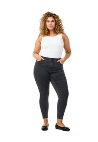 Mustat korkeavyötäröiset skinny-farkut, joissa on sileä pinta, etutaskut ja nilkkavetoketjut, yhdistettynä valkoiseen hihattomaan paita ja mustiin balettitossuihin.