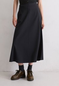 Jupe midi noire en tissu lisse, avec une taille haute et une silhouette en A. Assortie à des chaussettes texturées sombres et des chaussures marron.