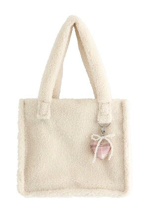 Kremfarvet fluffy tote-taske med tykke håndtag og en hængende lyserød ternet hjertecharme bundet med en hvid perlebue.