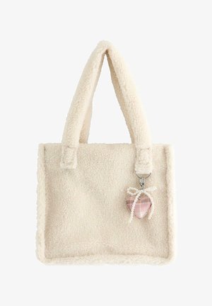 Kremfarvet fluffy tote-taske med tykke håndtag og en hængende lyserød ternet hjertecharme bundet med en hvid perlebue.