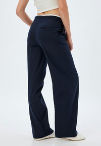 Pantalons larges bleu marine fabriqués en tissu doux, dotés d'une poche arrière et d'une taille élastique, présentés sur fond uni.