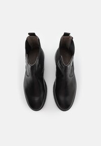 Bottes de cheville en cuir noir avec des panneaux latéraux élastiques, bout rond et une languette à l'arrière. Texture lisse avec des coutures décoratives.
