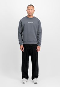 Pelēks sporta krekls ar ribotām piedurknēm un apakšmalu, ar baltu tekstu uz krūtīm. Kombinēts ar melnajiem platajiem biksēm un pelēkām sporta apaviem.