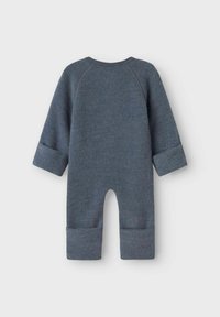 Une combinaison en tissu doux de couleur bleu foncé, à manches longues avec des poignets retroussés, présentant un col rond et un design à fond ouvert.