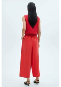 Suéter corto rojo con un acabado texturizado y un dobladillo con flecos, combinado con pantalones rojos de pierna ancha que cuentan con una cinturilla elástica y una textura suave.