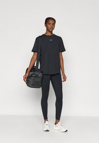 T-shirt noir Nike à manches courtes, associé à un legging noir et des baskets blanches. Un sac noir est porté en bandoulière.