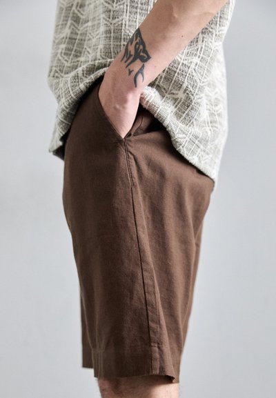Bruine linnen shorts met een relaxed fit, voorzien van zijzakken en een nette zoom. De stof heeft een subtiele textuur, wat het algehele uiterlijk verbetert.